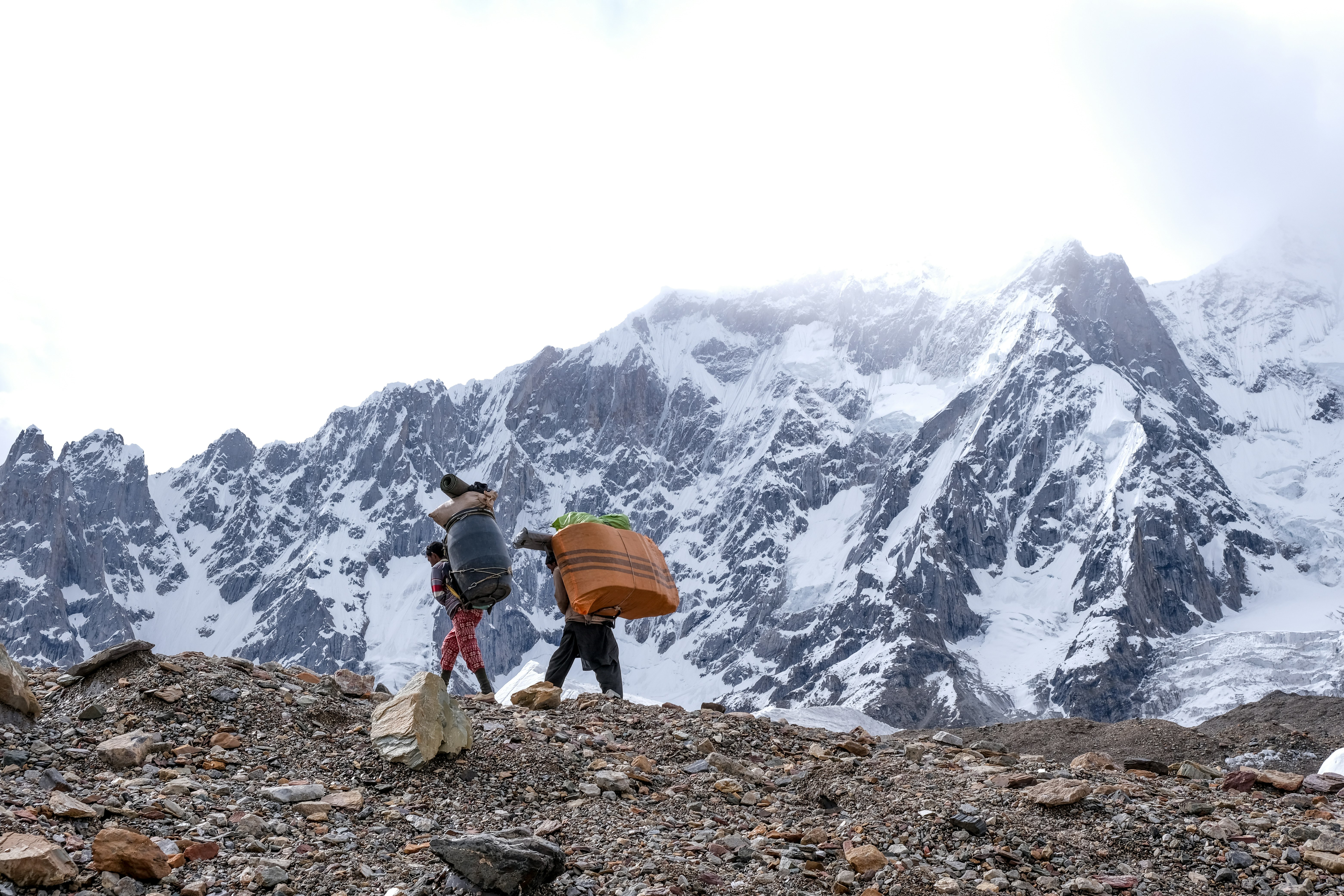 person in white jacket and brown pants carrying orange umbrella walking on rocky ground near snow